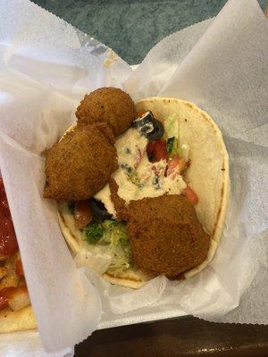 Falafel on pita bread, with hummus, lettuce, tomatoes, black olives, and tabbouleh.