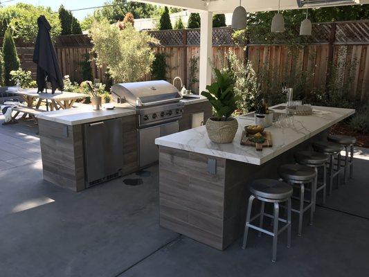 A two-island outdoor kitchen with bar seating. The island is faced with tile and the quartz counter top adds a nice touch.