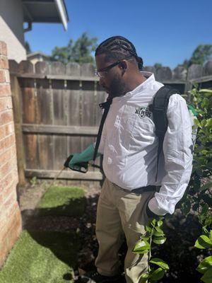 Pest control technician spraying treatment around the edges of the house's exterior