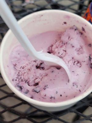 This is a half eaten single scoop of huckleberry ice cream.