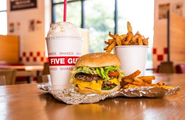 A Five Guys cheeseburger, milkshake and regular order of fries sits on a table inside a Five Guys restaurant.