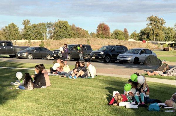 Participants in small family groups on lawn or stayed in or by their vehicles