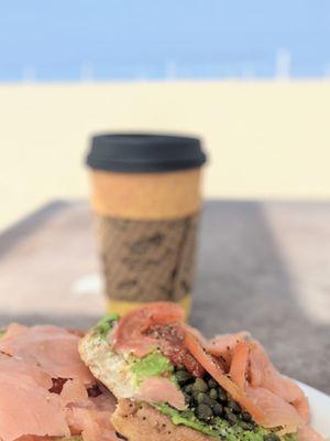 Bagel with lox and coffee enjoying it by the beach