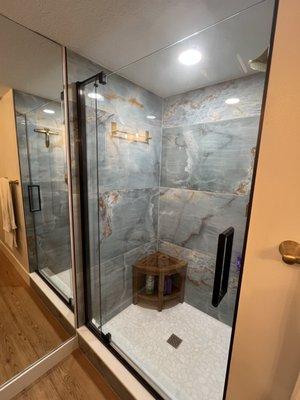 Porcelain large-format wall tile, natural stone mosaic shower floor, and Kohler shower door