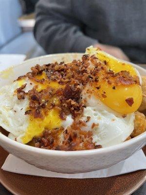 Tot Poutine, a bowl of crispy tator tots, breaded cheese curds, sausage gravy, over easy eggs, and real crumbled bacon.