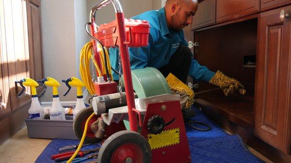 An Elite Rooter technician skillfully working under a sink, using specialized equipment to tackle a plumbing issue with precision.