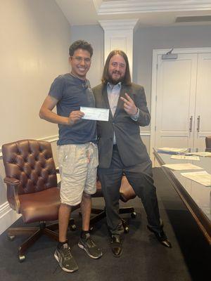 Zachary Clayton celebrates another win with a happy client, handing over a settlement check for their car accident case.