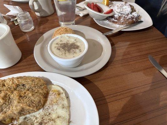 Biscuit and gravy for the chicken fried steak and on the right side is the cinnamon roll with a side of strawberries.