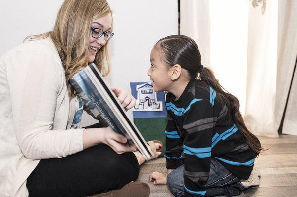 SLP Kaitlin makes speech therapy exercises fun with her client by reading a book and working on pronunciation.