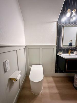 A sleek, minimalist half-bath with a wall-hung toilet and wainscoting. A clean, modern design with subtle elegance in a compact space.