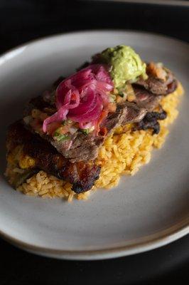 Platano Relleno: Tender steak over fried plantains, melted cheese, pico de gallo, pickled onions, guacamole, and rice for a bold twist.