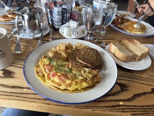 Omelette with sausage, toast and potatoes. On the side plate is pancakes and bacon