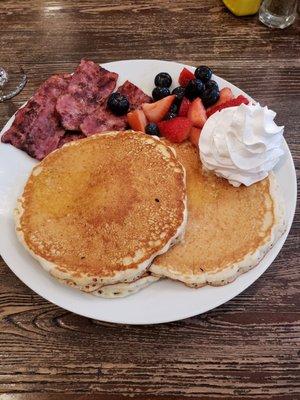 Pancakes with fruits and whip cream along with turkey bacon.