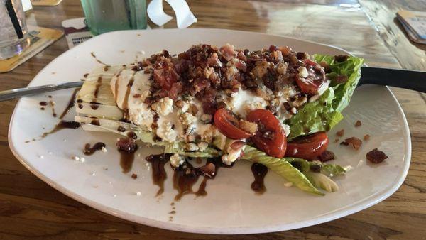 Wedge salad with tomatoes, bacon, dressing, and balsamic glaze.