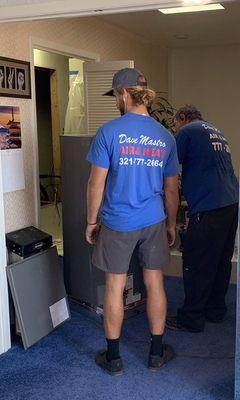 Two hard working men installing an air handler.