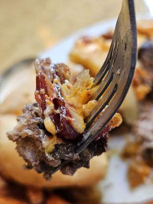 A fork holding a piece of the burger, bacon, onion ring, and cheese.