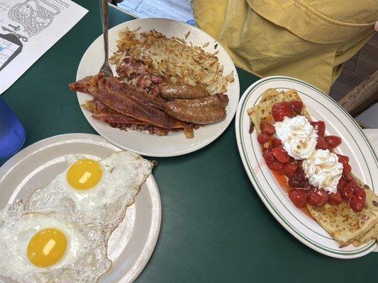 The Big Breakfast with sunny side up eggs, bacon, sausage, corned beef hash, and crepes with strawberries and whipped cream