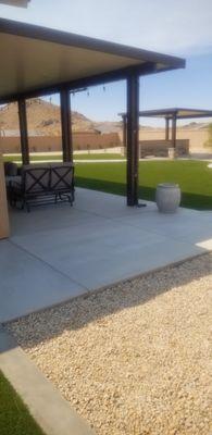 Foreground: covered patio, artificial turf, walking path leads to pergola covered gas fire pit with seating for 8 people.