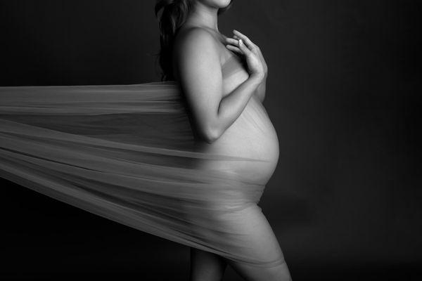 Black and white maternity portrait in profile with transparent fabric