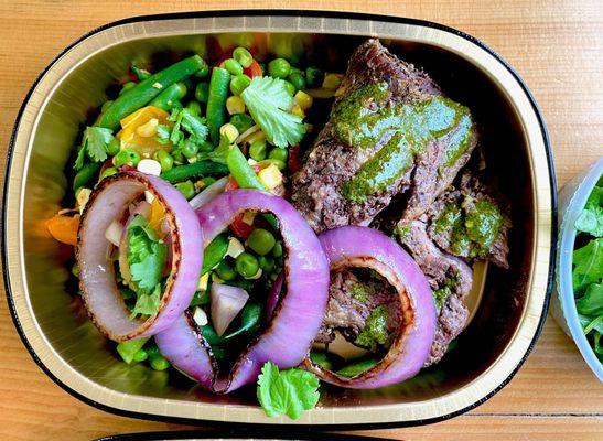 Individually packaged chimichurri steak over spring vegetable salad