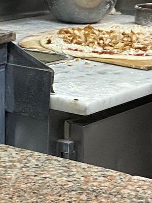 A cockroach on the corner of the counter where the pizza is being made.