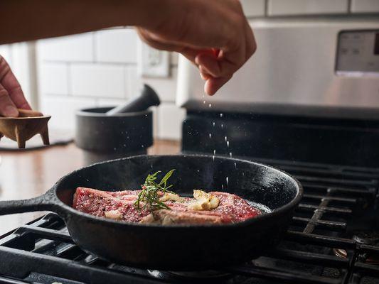 Houston ribeye steak cooking in a stovetop skillet