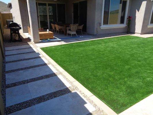 Travertine tile paver stepping pads with artificial turf back yard.