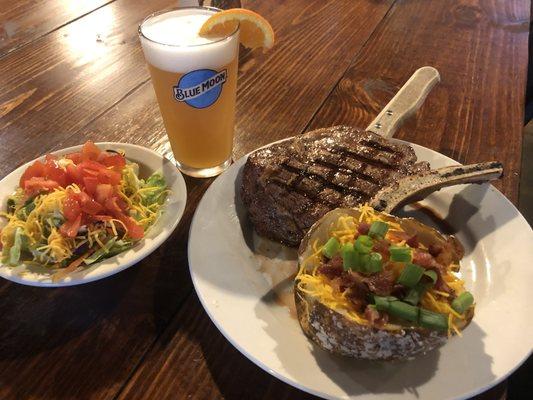 A bone-in pork chop served with a loaded baked potato and side salad