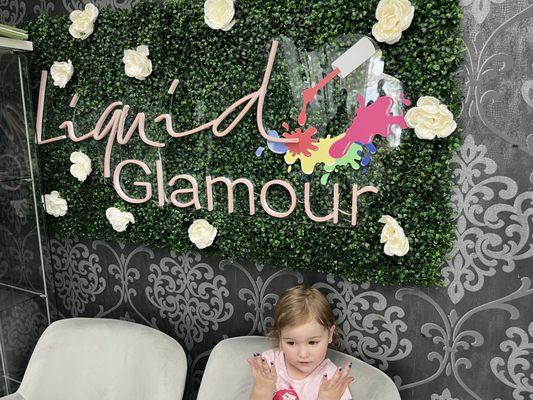 2 year old toddler with painted nails posing in front of stylish sign.