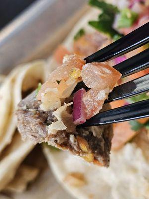 A fork holding a piece of the Flank Steak and other ingredients that had fallen from the Taco into the tray.