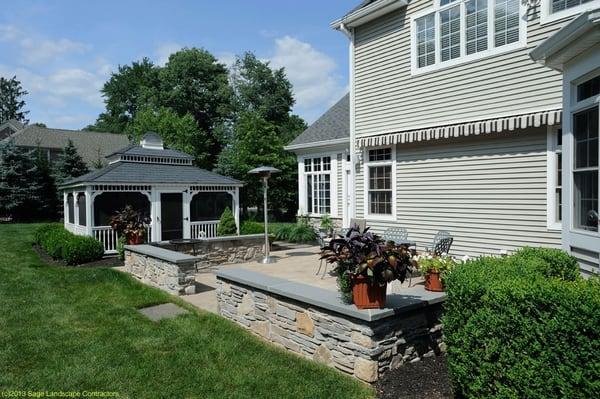 Lovely stone patio w/ decorative wall for seating, seasonal plantings and gazebo.