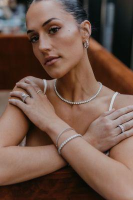 A woman wearing classic diamond jewelry including a tennis necklace, tennis bracelets, and wedding ring set