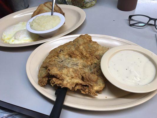 Chicken fried steak and eggs with toast, gravy, and grits.