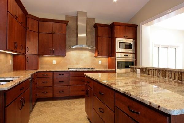 Kitchen with a curved, granite countertop island, stainless appliances and cherry cabinets.