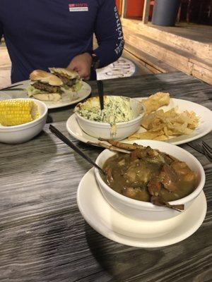 Cup of gumbo, half eaten spinach dip, & hamburger with a side of corn