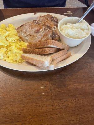 Pork chops with scrambled eggs, grits and toast.