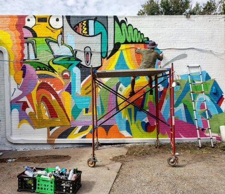 Mural artist sitting on scaffold for Plaza Walls Mural Expo 2019