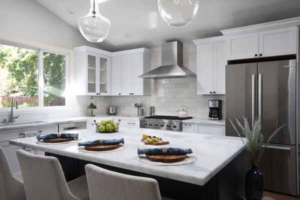 Bright and modern kitchen with white cabinetry, stainless steel appliances, large marble island, and cozy seating. Ideal for entertaining!