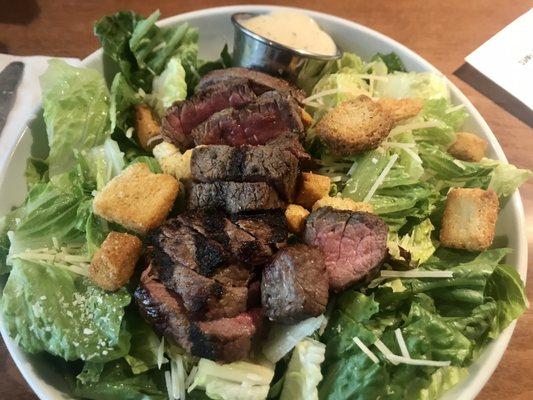 Caesar salad with steak and side dressing.