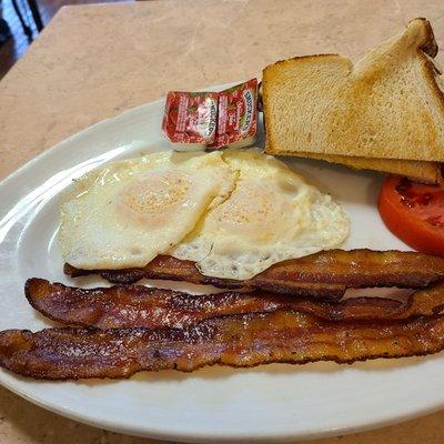 Two fried eggs over medium with bacon and white toast.