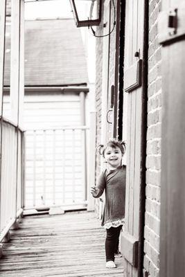 Toddler girl looks out from French door in New Orleans. Black and white photograph