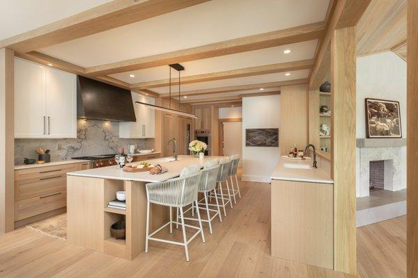 Custom Kitchen with white oak cabinetry and beams, steel hood, outdoor rated counter stools and a slab backsplash.