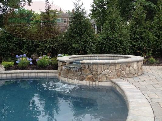 Jacuzzi detail, part of a in-ground free-form pool showcasing natural stone with waterfall feature, bullnose coping and paver stone decking.