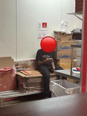 Employee sitting on top of pizza to-go boxes playing on his phone.