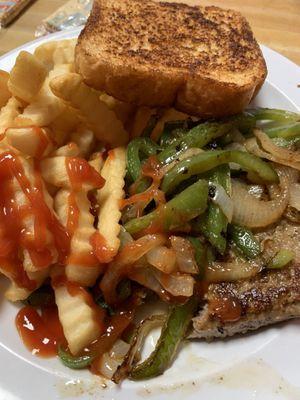 Hamburger steak plate with peppers and onions a side of fries, salad and toast.