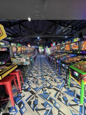 Row of pinball machines looking down the center of the arcade.