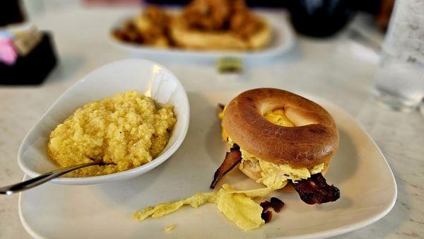 Eggs with cheese, bacon on a bagel with a side of grits