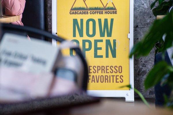 "Now open" sandwichboard sign; booth in back, shot taken from small table