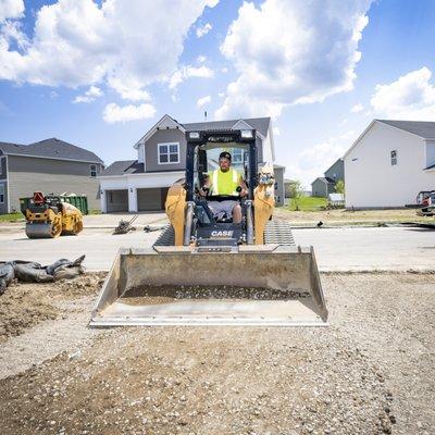 Skid steer operator smoothing out the base material and prepping for asphalt.