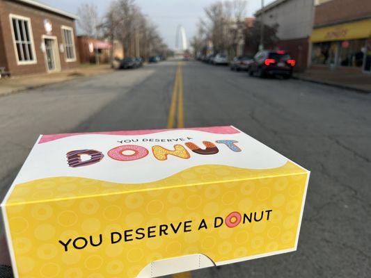 John's donut box that says "you deserve a donut" with the St. Louis arch in the background.